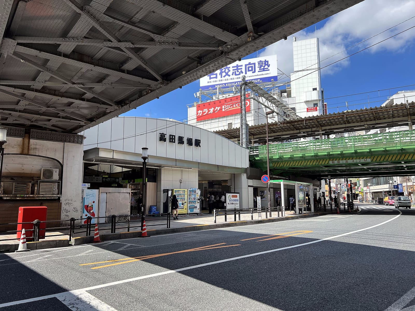高田馬場駅の駅舎入口と、道路をまたぐ緑色の鉄道高架橋。